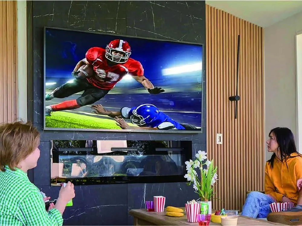 An outdoor television mounted in a covered alfresco entertaining area with people watching sport